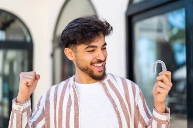 Handsome Arab man holding invisible braces at outdoors celebrating a victory