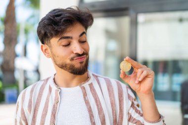 Handsome Arab man holding a Bitcoin at outdoors with sad expression
