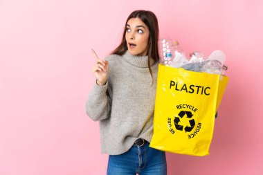 Young caucasian woman holding a bag full of plastic bottles to recycle isolated on pink background intending to realizes the solution while lifting a finger up
