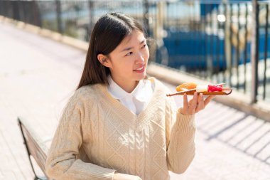 Young Chinese woman holding sashimi at outdoors looking up while smiling