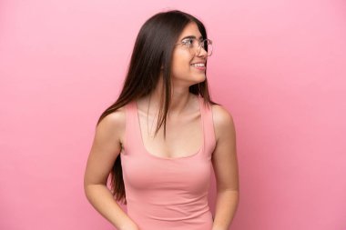 Pembe arka planda soyutlanmış genç beyaz kadın yana bakıyor ve gülümsüyor.