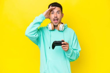 Young handsome man playing with a video game controller over isolated wall with surprise expression