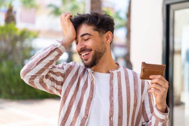 Handsome Arab man holding a wallet at outdoors has realized something and intending the solution