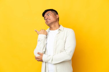Young Ecuadorian man isolated on yellow background pointing to the side to present a product
