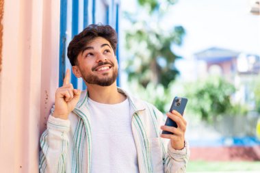 Handsome Arab man using mobile phone at outdoors intending to realizes the solution while lifting a finger up