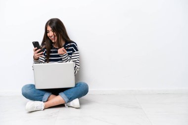 Yerde dizüstü bilgisayarlı beyaz bir kadın oturuyor. Beyaz arka planda izole edilmiş. Şaşırdı ve bir mesaj gönderiyor.