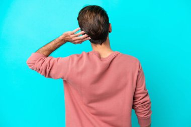 Kafkasyalı genç adam mavi arka planda izole edilmiş ve düşünüyor.