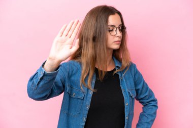 Pembe arka planda izole edilmiş genç beyaz kadın dur hareketi yapıyor ve hayal kırıklığına uğruyor.