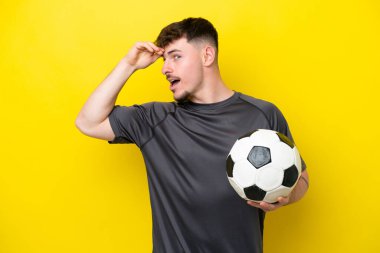 Sarı arka planda izole edilmiş genç futbolcu yan tarafa bakarken sürpriz jest yapıyor.