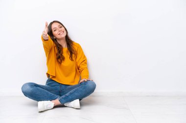 Young caucasian woman sitting on the floor isolated on white wall shaking hands for closing a good deal