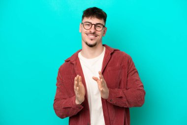 Beyaz tenli yakışıklı adam mavi arka planda izole edilmiş bir konferansta sunumdan sonra alkışlıyor.