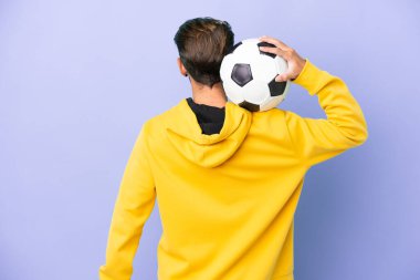 Mor arka planda futbol topuyla izole edilmiş genç beyaz bir adam.