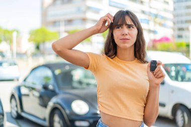 Dışarıda arabanın anahtarlarını tutan genç bir kadın. Şüpheleri var ve kafası karışmış bir yüz ifadesi var.