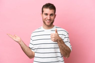 Kafkasyalı genç adam pembe arka planda izole edilmiş. Kopyalama alanı hayali bir şekilde avucunun içinde duruyor. Bir ilan vermek için.