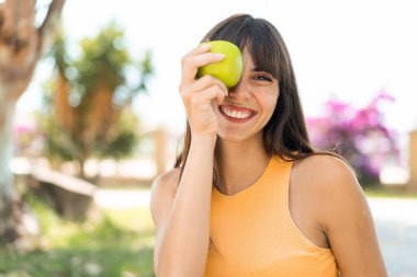 Açık havada elinde mutlu bir ifadeyle elma tutan genç bir kadın.