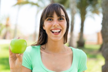 Açık havada elmalı genç bir kadın. Şaşırmış ve şok olmuş bir yüz ifadesi var.