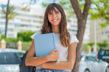 Dışarıda elinde bir defter tutan genç bir kadın.