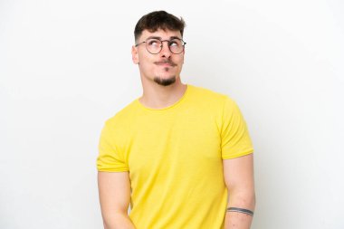Beyaz arka planda izole edilmiş beyaz, yakışıklı genç bir adam yukarı bakarken şüphe duyuyor.