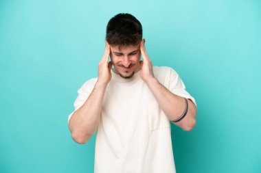 Kafkasyalı yakışıklı genç adam mavi arka planda başağrısı ile izole edilmiş.