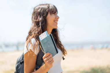 Açık havada elinde mutlu bir ifadeyle pasaport tutan genç bir kadın.