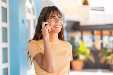 Dışarıda genç bir kadın cep telefonuyla birileriyle sohbet ediyor.