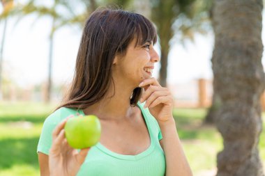 Açık havada elmalı genç bir kadın bir fikir üretiyor ve ona bakıyor.