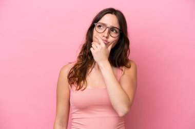 Pembe arka planda izole edilmiş genç, beyaz bir kadın. Şüpheleri var ve kafası karışmış bir yüz ifadesi var.