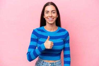 Pembe arka planda izole edilmiş beyaz bir kadın baş parmak hareketi yapıyor.