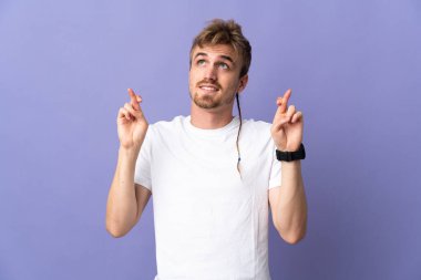 Mor arka planda izole edilmiş genç, yakışıklı sarışın adam, şans diliyor ve en iyisini diliyor.