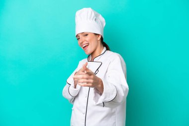 Young caucasian chef woman isolated on blue background pointing to the front and smiling