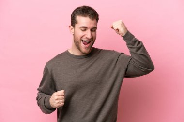 Pembe arka planda izole edilmiş genç beyaz bir adam zaferi kutluyor.