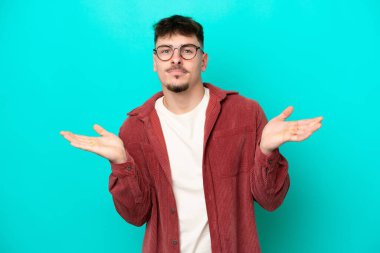 Young caucasian handsome man isolated on blue background having doubts while raising hands
