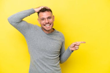 Sarı arka planda izole edilmiş, genç, beyaz, yakışıklı bir adam. Şaşırmış ve işaret ediyor.