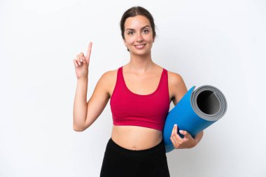 Beyaz arka planda izole edilmiş bir minderi tutarak yoga derslerine giden beyaz bir kadın harika bir fikre işaret ediyor.