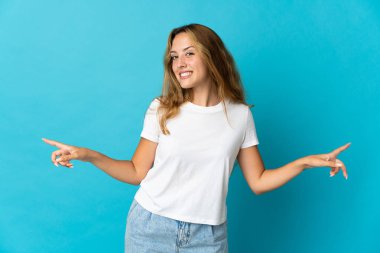 Mavi arka planda izole edilmiş genç sarışın kadın parmak uçlarında ve mutlu.