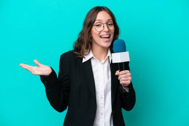 Young TV presenter woman isolated on blue background with shocked facial expression