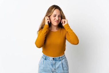 Mavi arka planda izole edilmiş genç sarışın kadın hayal kırıklığına uğramış ve kulaklarını kapatmış.