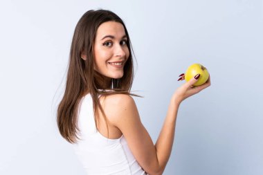 Soyutlanmış mavi arka planda elma yiyen genç bir kadın.