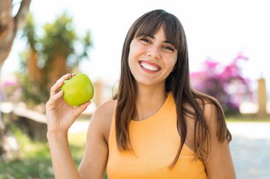 Açık havada elinde mutlu bir ifadeyle elma tutan genç bir kadın.