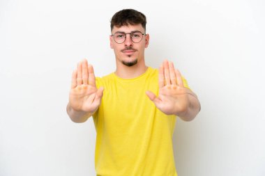 Beyaz arka planda izole edilmiş beyaz tenli yakışıklı genç adam dur hareketi yapıyor ve hayal kırıklığına uğruyor.