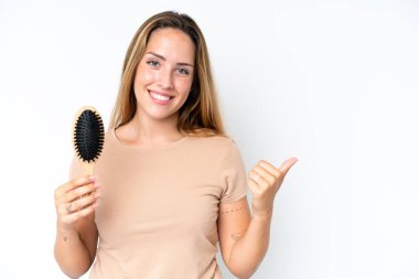 Young caucasian woman with hair comb isolated on white background pointing to the side to present a product