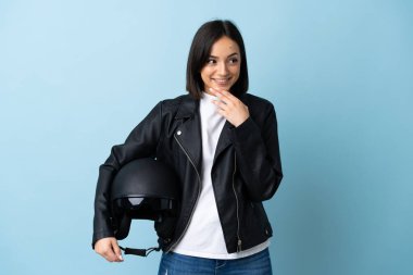 Woman holding a motorcycle helmet isolated on blue background looking up while smiling