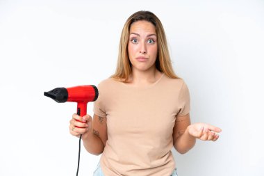 Young caucasian woman holding a hairdryer isolated on white background making doubts gesture while lifting the shoulders