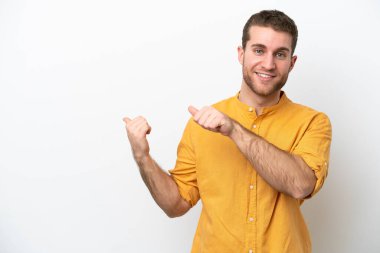 Beyaz arka planda izole edilmiş genç beyaz bir adam bir ürün sunmak için kenarı işaret ediyor.