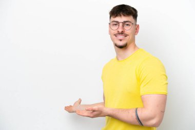 Beyaz arka planda soyutlanmış beyaz tenli yakışıklı adam, davet edilmek için ellerini yana uzatıyor.