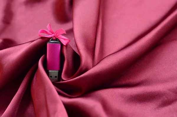 明亮的粉红色 Usb 闪存卡与弓躺在一个毯子红色地图集织物与很多救济褶皱 女性设计中的内存存储设备 — 图库照片