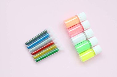 Renkli pırıltılar pastel pembe arka plan üzerinde yatıyor. Oje için çok renkli parlak ışıltılar ile birçok yuvarlak kavanoz. Köpüklü payetler