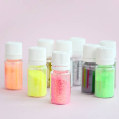 Renkli pırıltılar pastel pembe arka plan üzerinde yatıyor. Oje için çok renkli parlak ışıltılar ile birçok yuvarlak kavanoz. Köpüklü payetler