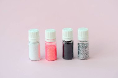 Renkli pırıltılar pastel pembe arka plan üzerinde yatıyor. Oje için çok renkli parlak ışıltılar ile birçok yuvarlak kavanoz. Köpüklü payetler