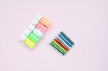 Renkli pırıltılar pastel pembe arka plan üzerinde yatıyor. Oje için çok renkli parlak ışıltılar ile birçok yuvarlak kavanoz. Köpüklü payetler